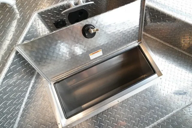 Slide: The Image of An open storage compartment on a 2027 Lund 185 Heavy Gauge Sport boat, featuring a diamond-patterned floor. - 39