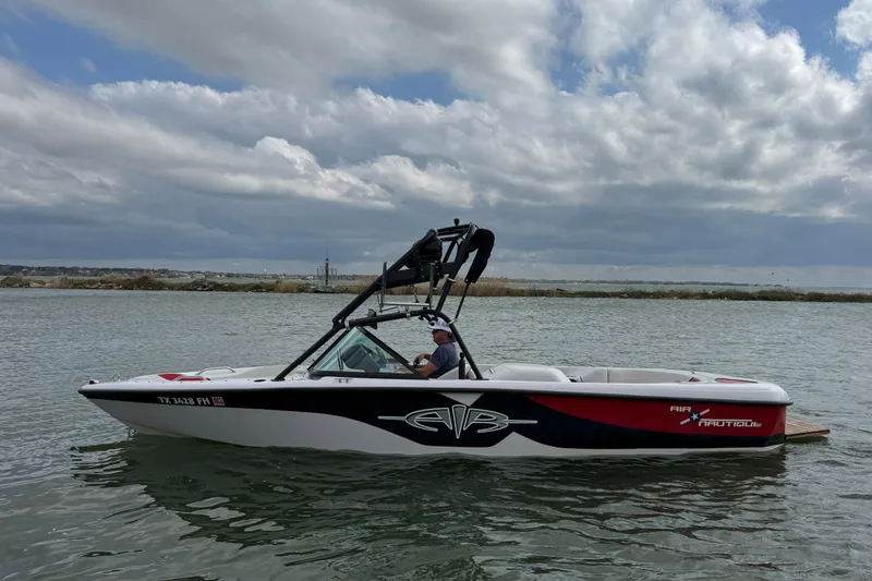 The Image of 2000 Correct Craft Super Air Nautique boat on a calm lake under cloudy skies. - 1