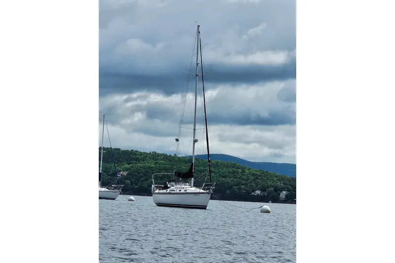 Slide: The Image of 1985 Hunter 31 sailboat anchored on a lake with cloudy skies and lush green hills. - 4