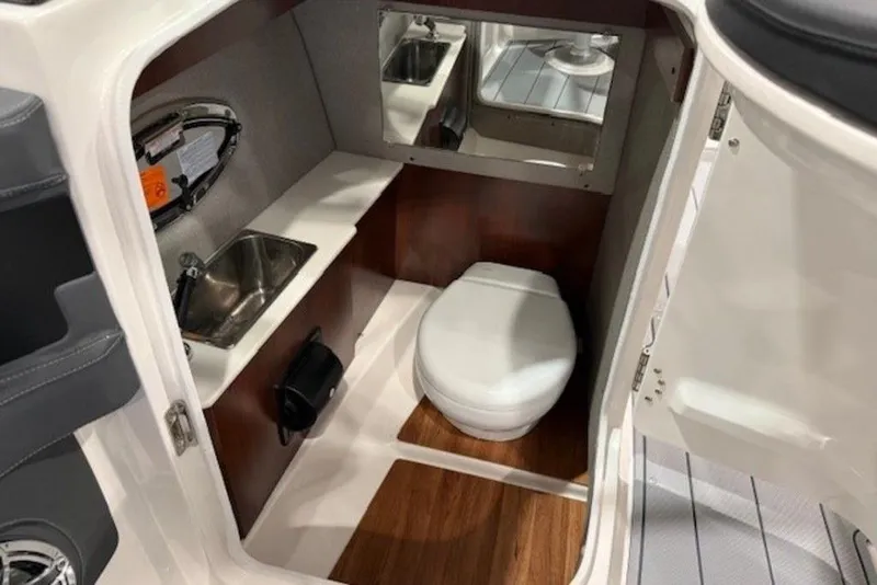 Slide: The Image of 2026 Chaparral 270 OSX boat interior with compact bathroom, featuring a toilet and sink. - 13