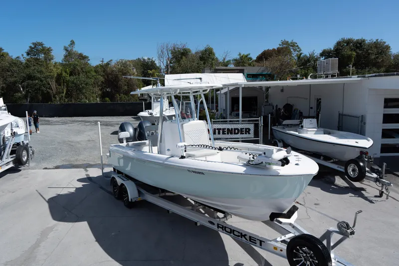 Slide: The Image of 2023 Contender 24 Sport boat on trailer, parked outdoors near trees and buildings. - 2