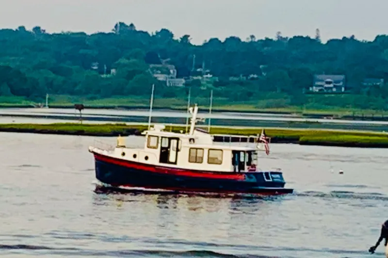 The Image of 2002 Nordic Tug 37 cruising on a serene river with lush green background. - 1