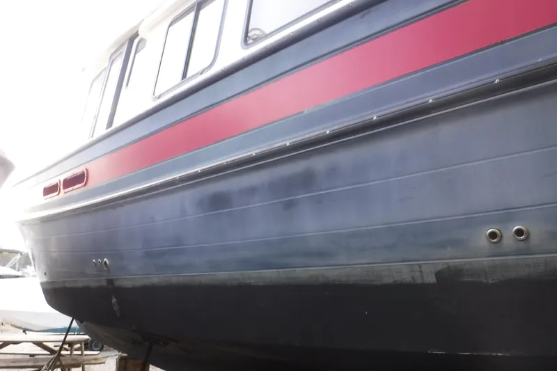 Slide: The Image of 2002 Nordic Tug 37 boat hull with red stripe, docked on land. - 4