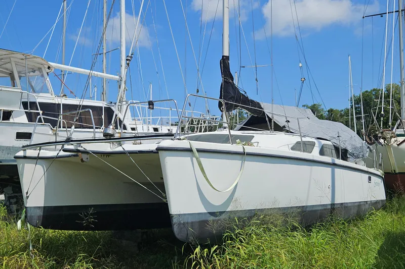 Slide: The Image of 2005 Gemini MC 105 catamaran on land, surrounded by grass and other boats. - 37