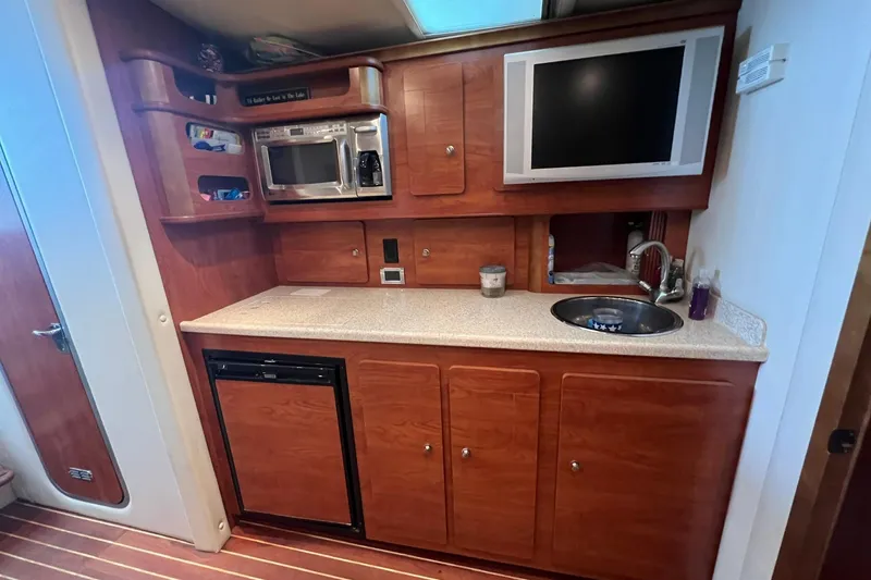 Slide: The Image of 2008 Rinker 400 Express Cruiser galley with microwave, sink, TV, and wooden cabinetry. - 11
