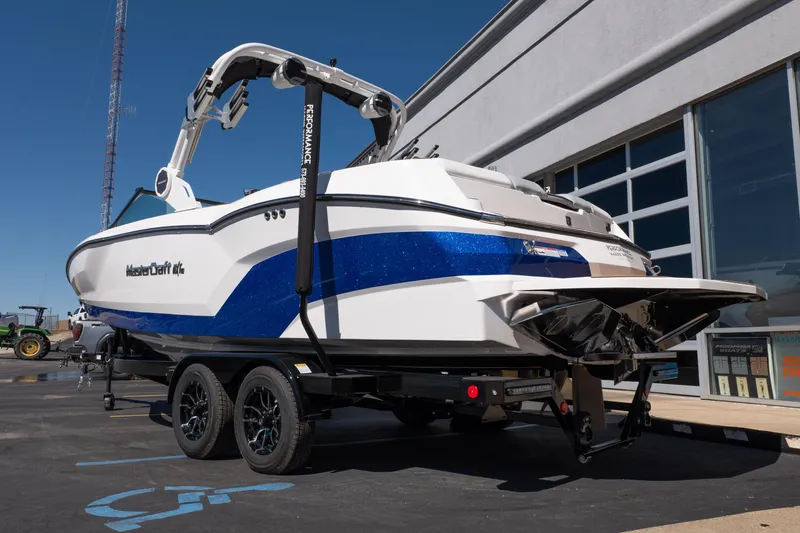 Slide: The Image of 2026 MasterCraft NXT24 boat on trailer, white and blue design, parked outside a building. - 3