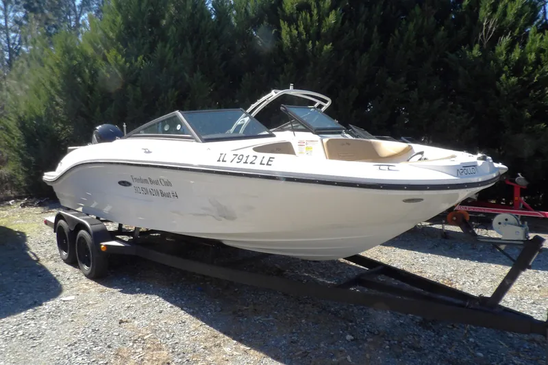 Slide: The Image of 2023 Searay 210 SPO boat on trailer, parked outdoors with trees in background. - 2