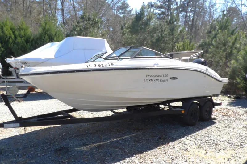 Slide: The Image of 2023 Searay 210 SPO boat on trailer, parked outdoors with trees in background. - 3