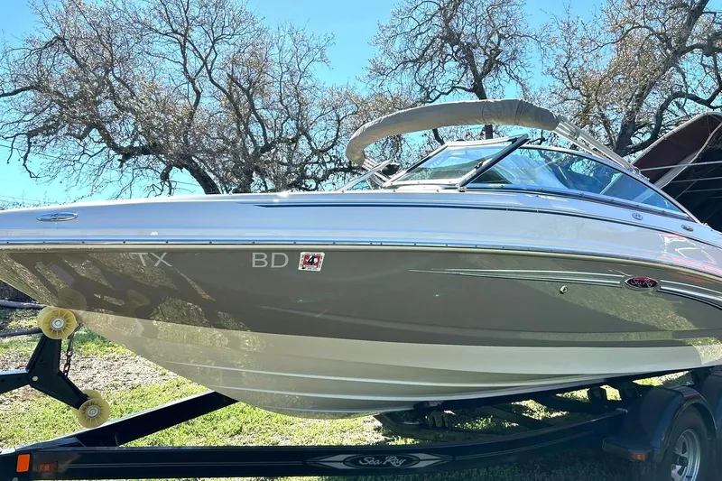 Slide: The Image of 2009 Sea Ray 210 boat on trailer, parked outdoors with trees in background. - 13