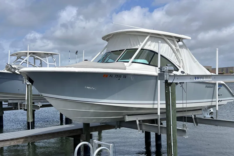 Slide: The Image of 2022 Pursuit DC 246 Dual Console boat docked on a lift under cloudy skies. - 9
