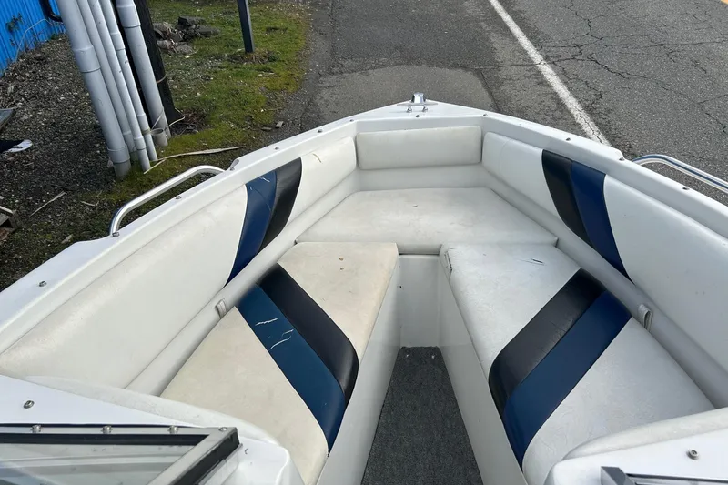 Slide: The Image of 1995 Reinell 18 BRXL boat interior with white and blue seating, parked on roadside. - 7