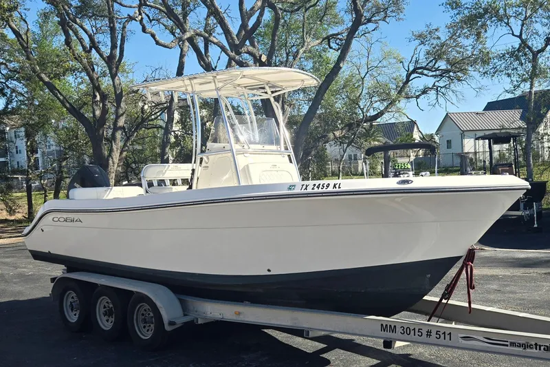 The Image of 2022 Cobia 237 Center Console boat on trailer, parked outdoors with trees in background. - 1
