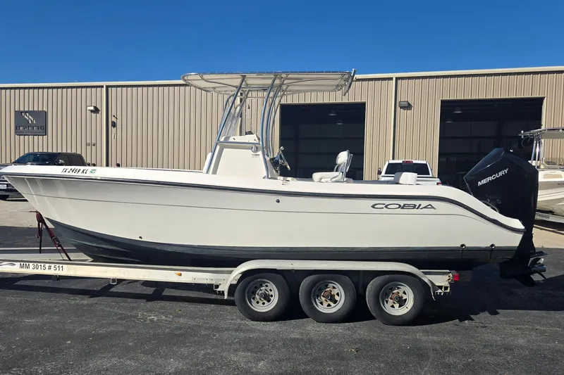 Slide: The Image of 2022 Cobia 237 Center Console boat on trailer, parked outside a warehouse. - 7