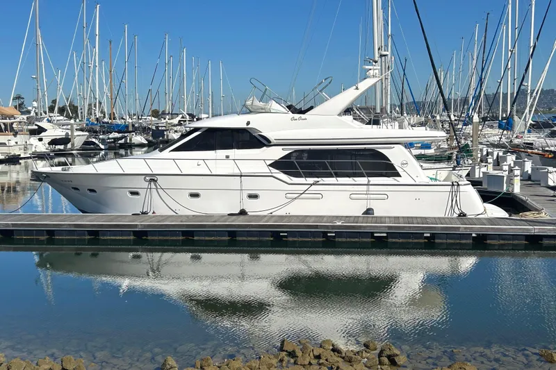 The Image of 1998 Bayliner 5788 Pilot House Motoryacht docked in a marina, surrounded by sailboats. - 0