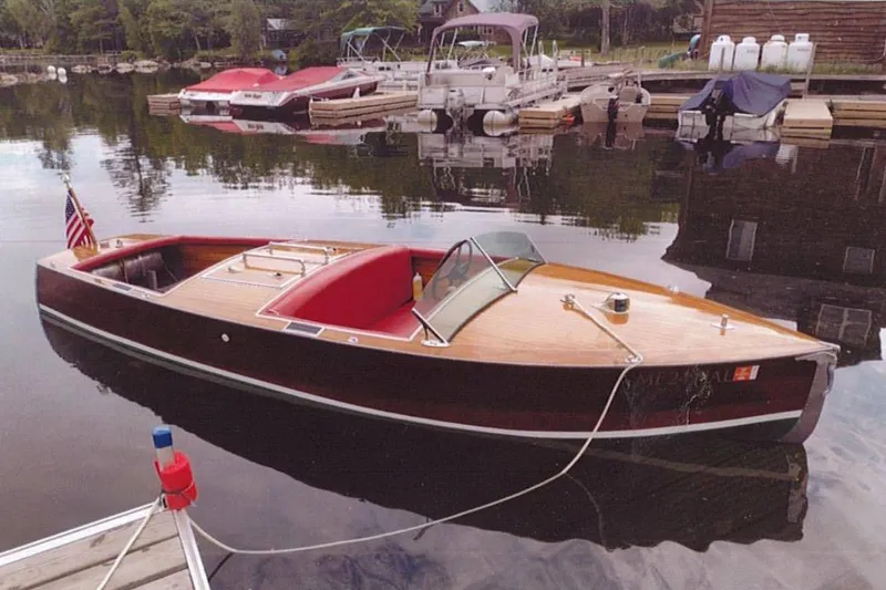 The Image of 1931 Dodge 16' Sea Nymph boat docked on a calm lake with scenic background. - 0
