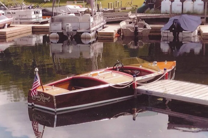 Slide: The Image of 1931 Dodge 16' Sea Nymph boat docked at a marina, featuring classic wooden design. - 2