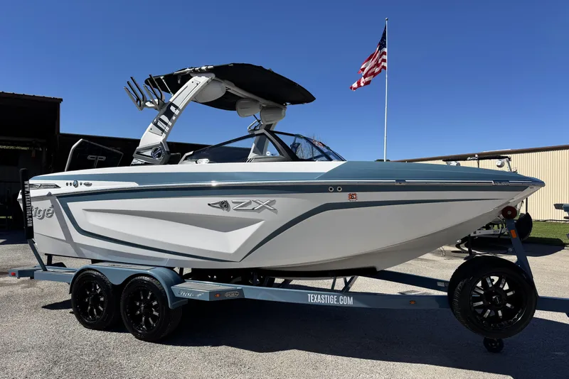 The Image of 2021 Tigé 21ZX boat on trailer, sleek design, American flag in background. - 1
