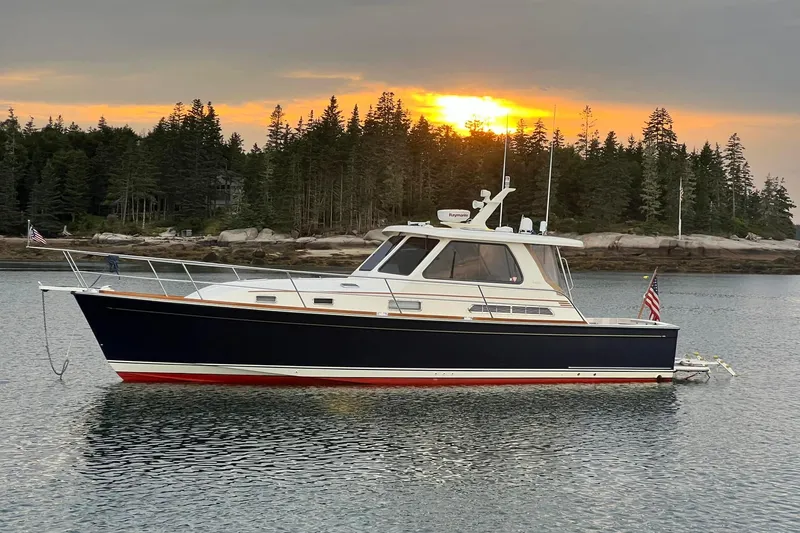 The Image of 2006 Sabre 38 Hard Top Express boat on calm water at sunset, forested shoreline in background. - 1