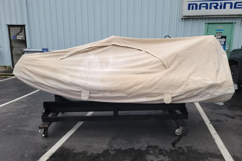 Slide: The Image of 2023 Highfield Sport 330 boat covered, parked on a wheeled stand outside a marine shop. - 17