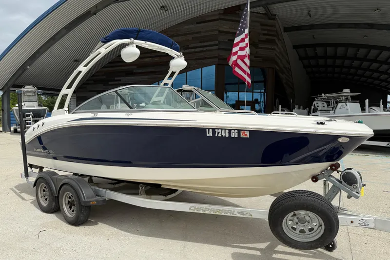 Slide: The Image of 2016 Chaparral H20 21 Deluxe boat on trailer, parked outside a building with American flag. - 2