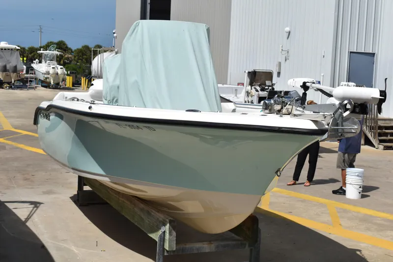Slide: The Image of 2022 Key West 219 FS boat in a marina, partially covered, with nearby equipment. - 2