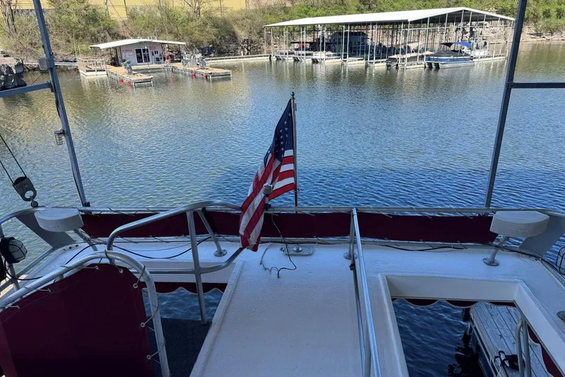 Slide: The Image of 1987 Stardust Cruisers houseboat with American flag, docked on a serene lake. - 59