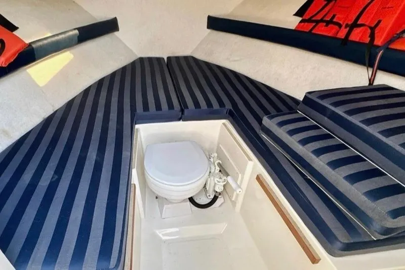 Slide: The Image of Interior of 2001 Pursuit 2460 Denali boat with striped cushions and a compact toilet. - 5