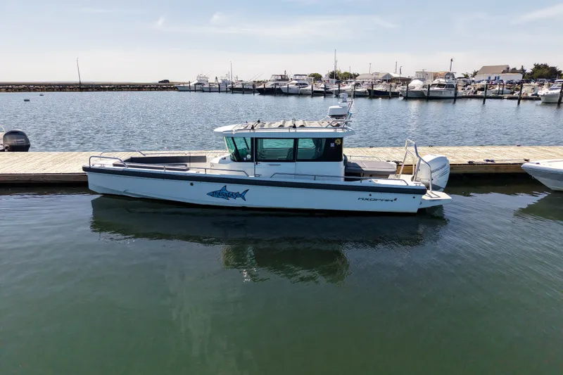 Slide: The Image of 2020 Axopar 28 Cabin boat docked at a marina, calm water, clear sky. - 1