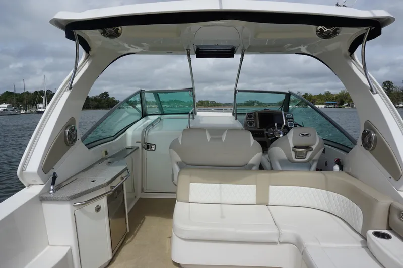 Slide: The Image of 2014 Chaparral 330 Signature boat interior with seating, helm, and kitchenette on a calm waterway. - 11