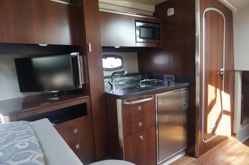Slide: The Image of 2014 Chaparral 330 Signature yacht interior with kitchenette, TV, and wood cabinetry. - 32