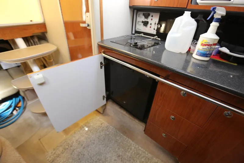 Slide: The Image of 2000 Chaparral Signature 300 boat interior kitchen with open cabinet, stove, and cleaning supplies. - 31
