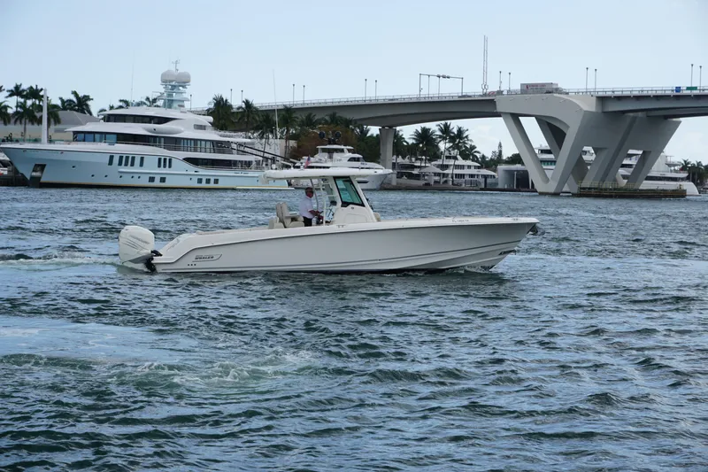 Slide: The Image of 2018 Boston Whaler 330 Outrage cruising near a bridge with yachts in the background. - 12