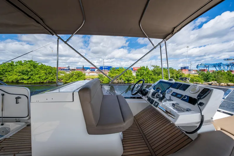 Slide: The Image of 2012 Prestige Flybridge yacht helm with modern controls, overlooking lush greenery and industrial backdrop. - 36