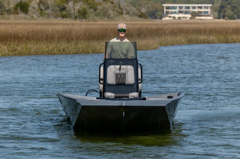Slide: The Image of 2026 Excel 220 Bay Pro Elite boat on water, person steering, marshland background. - 2