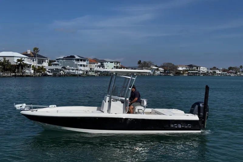 Slide: The Image of 2015 Robalo 226 Cayman boat cruising on a calm waterfront with houses in the background. - 19
