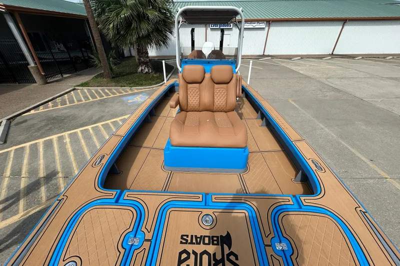 Slide: The Image of 2026 Skuta 24 Skuta Cat boat with tan and blue deck, parked outdoors. - 19