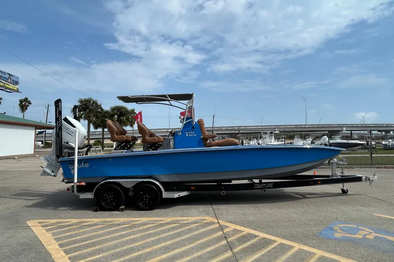 Slide: The Image of Blue 2026 Skuta 24 Skuta Cat boat on trailer, parked outdoors under a cloudy sky. - 2