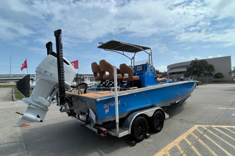 Slide: The Image of 2026 Skuta 24 Skuta Cat boat on trailer, blue exterior, parked outdoors. - 4