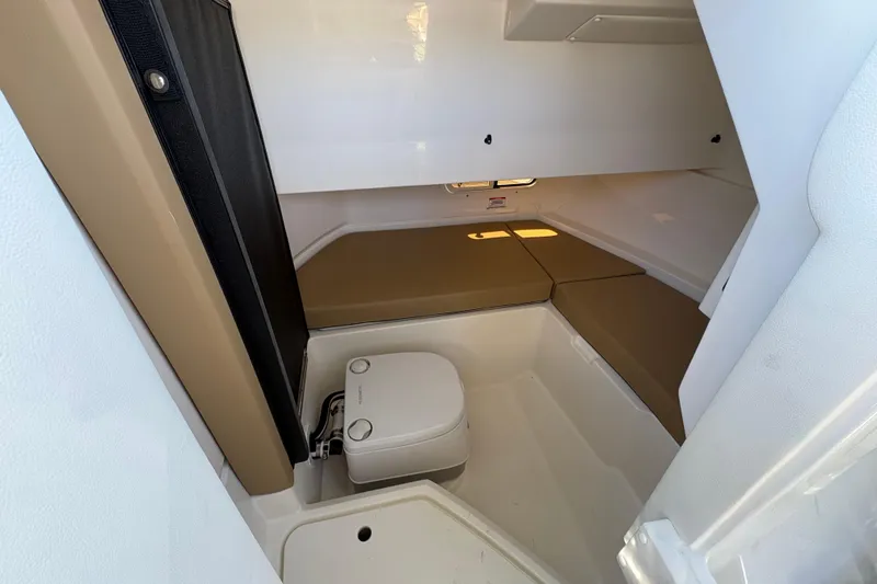Slide: The Image of 2024 Sea Ray SDX 250 Outboard cabin interior with compact toilet and seating area. - 18