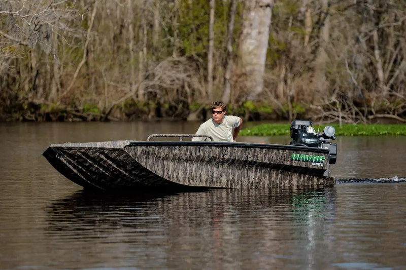 Slide: The Image of Man driving 2026 Havoc 1756 MSTC boat on a calm river with wooded background. - 13