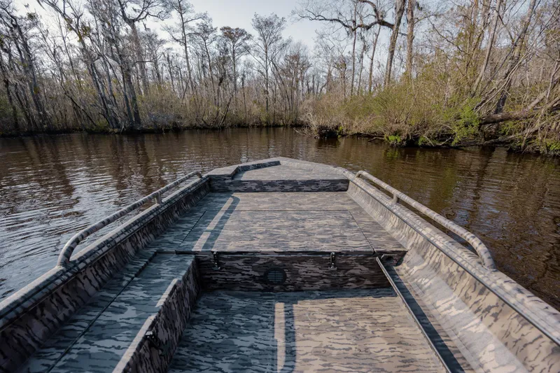 Slide: The Image of Camouflage-patterned Havoc 1756 MSTC boat navigating a serene, wooded waterway. - 14