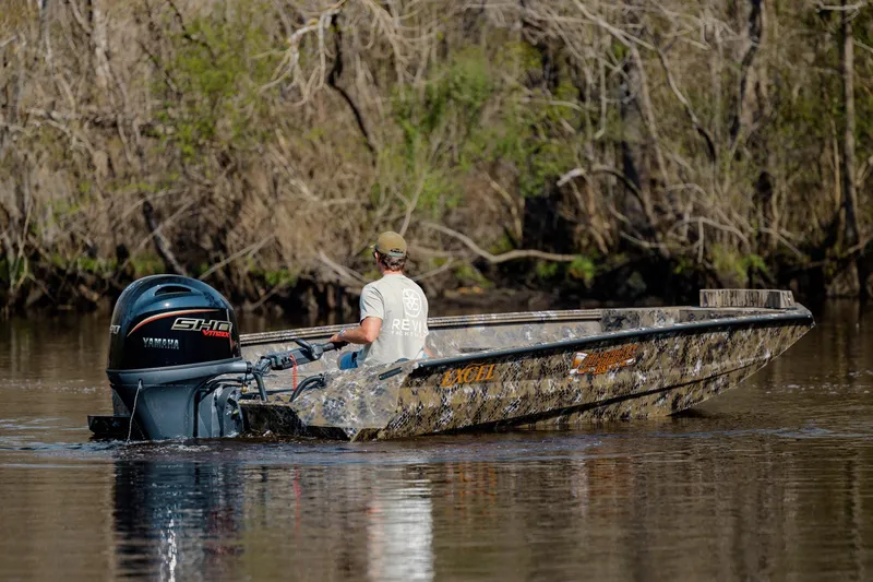 Slide: The Image of Man operating Excel 183 Tomahawk boat on a calm river, surrounded by trees. - 10