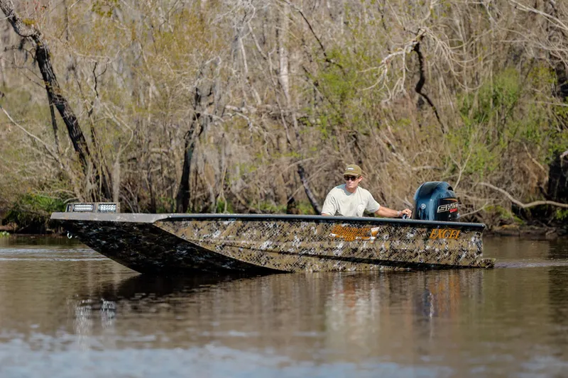 Slide: The Image of Man operating Excel 183 Tomahawk boat on a calm river, surrounded by trees. - 11