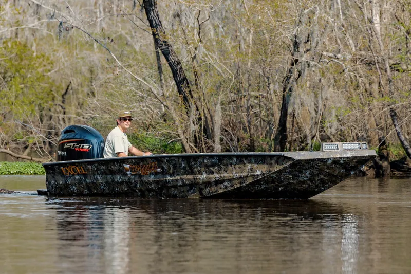 Slide: The Image of 2026 Excel 183 Tomahawk boat navigating a calm river with trees in the background. - 13