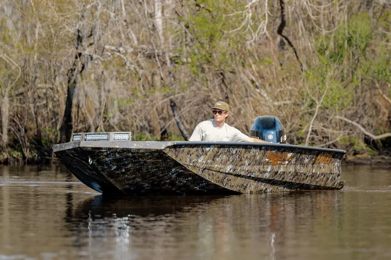 Slide: The Image of Man navigating Excel 183 Tomahawk boat on a calm river, surrounded by trees. - 14