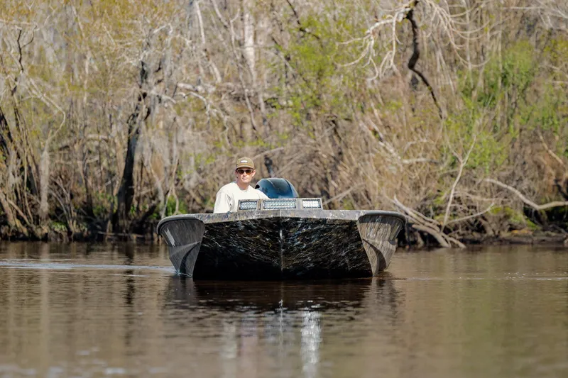 Slide: The Image of Man navigating Excel 183 Tomahawk boat on a calm river, surrounded by trees. - 15