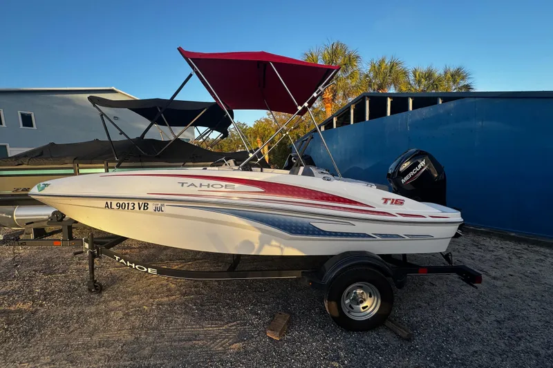 Slide: The Image of 2024 Tahoe T16 boat with red canopy on trailer, parked outdoors. - 8