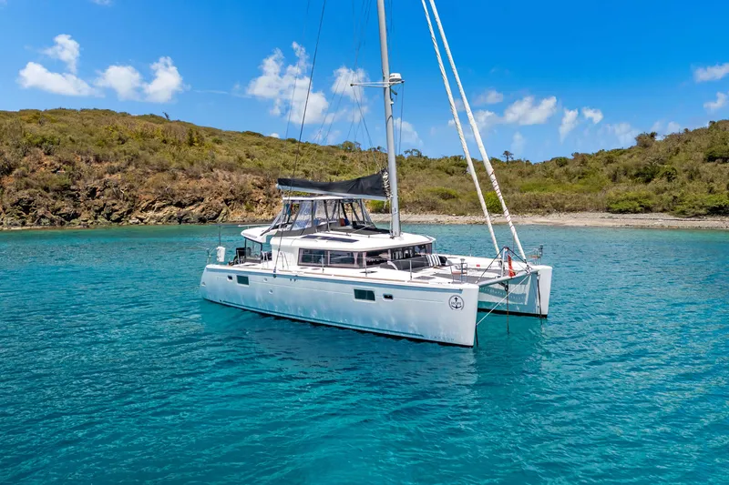 Slide: The Image of 2017 Lagoon 450 F catamaran anchored in clear blue water near a lush coastline. - 4