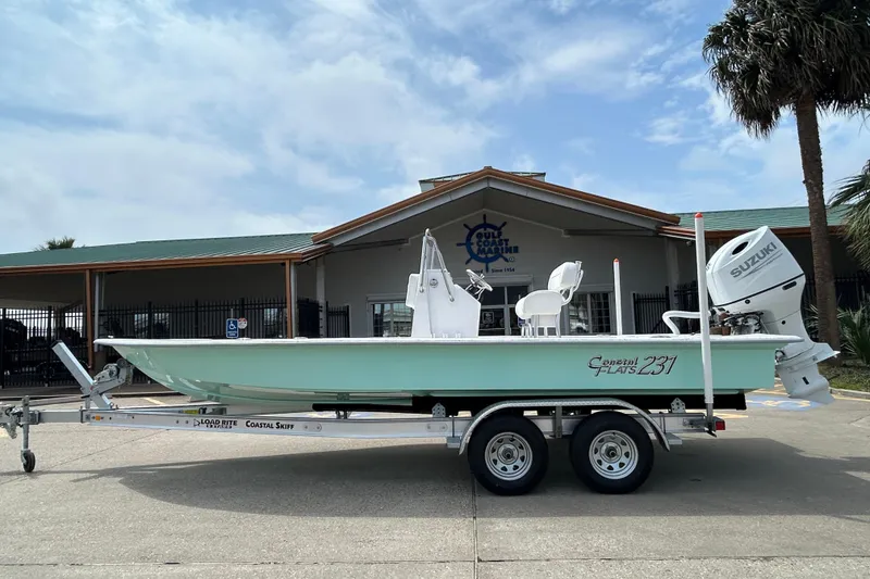 The Image of 2026 Coastal Skiff 231 Flats boat on trailer, parked outside a marine store. - 0