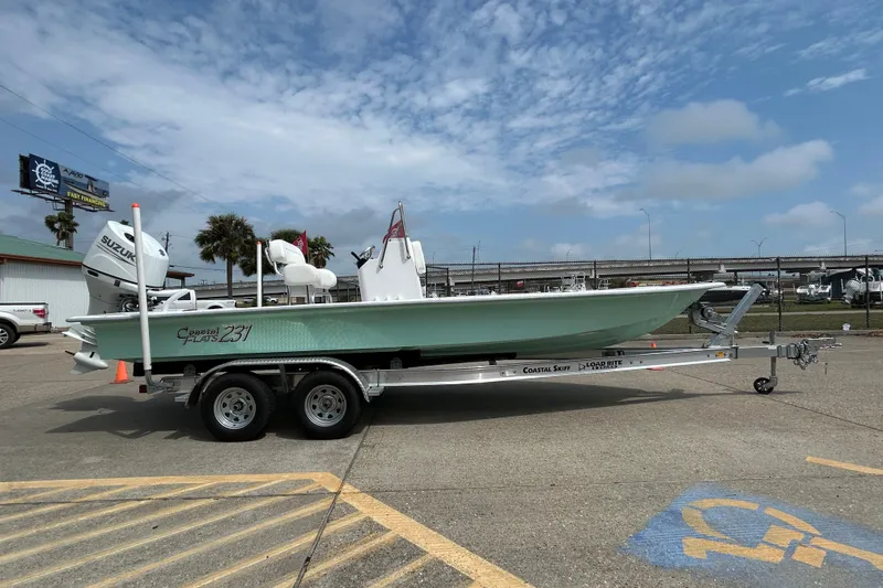 Slide: The Image of 2026 Coastal Skiff 231 Flats boat on trailer, parked outdoors under a cloudy sky. - 2